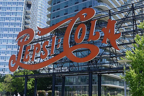 The Pepsi-Cola sign close up, red script letters on a steel frame with a glass apartment tower directly behind it.