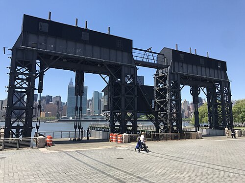 The two gantries on the waterfront, black steel with their hoist houses on top and Midtown Manhattan between the legs.