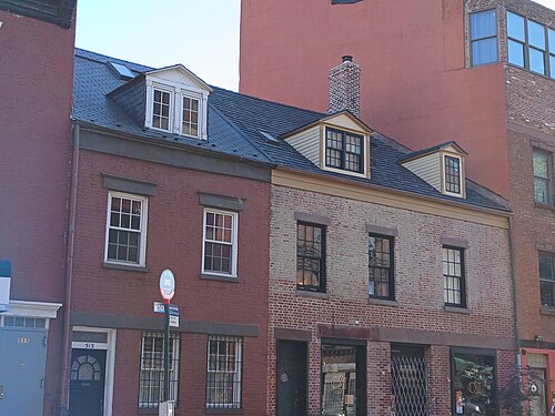 Two low brick houses at 511 and 513 Grand Street, three dormer windows in a slate roof and shopfronts at street level, with a taller building alongside.