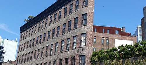 A five storey brick warehouse building shot at an angle against a clear sky, a cornice along its roofline and a plain rooftop addition set back behind it.