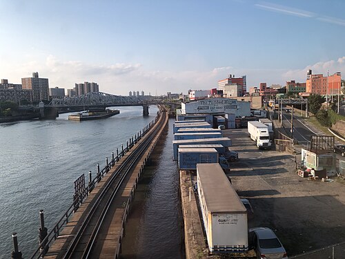 A truck yard and moving company depot along the Harlem River, the Oak Point Link freight line at the water's edge and a swing bridge beyond.