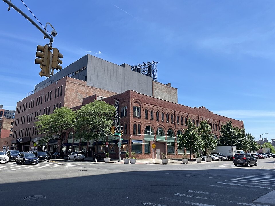 The corner of Lincoln Avenue and Bruckner Boulevard, low brick factory era buildings with round arched windows and storefronts at the sidewalk.