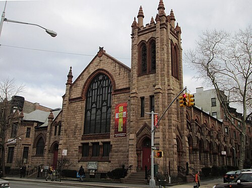 Grace United Methodist Church on the corner of Seventh Avenue and St John's Place, brownstone with a square tower, the parsonage and a row of houses beside it.