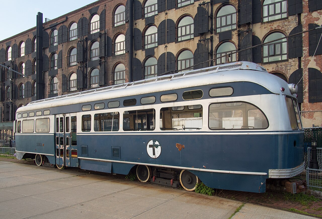 One of the Beard Street warehouses, four floors of brick with arched windows and black iron shutters, an old Boston streetcar standing on rails in front of it.