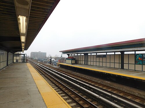 The elevated platforms at Beach 90th Street on a misty day, the station sign with the Holland name on it, small houses and a church steeple below.
