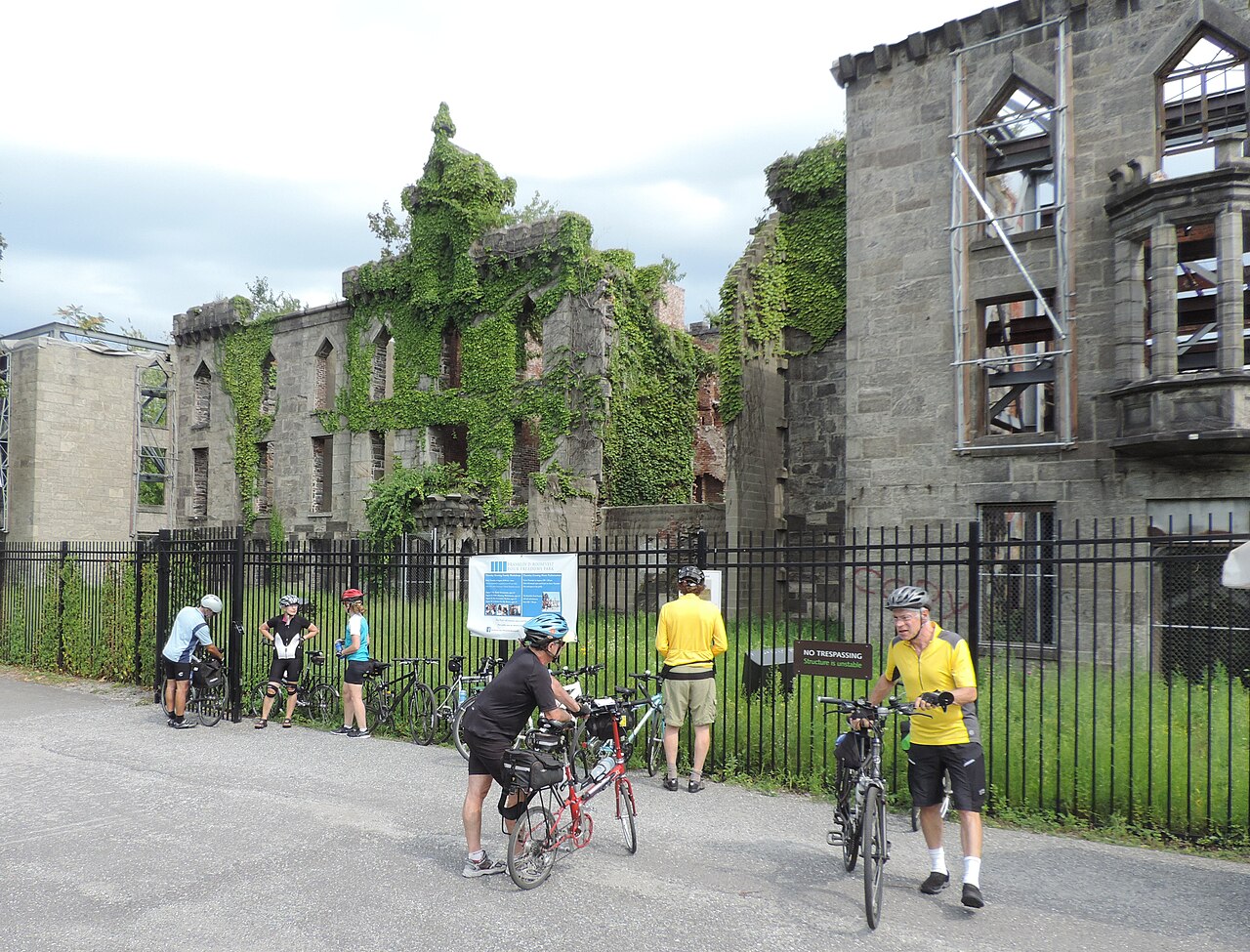 The Smallpox Hospital ruin, ivy over grey stone and empty window openings, one wing held up by scaffolding behind an iron fence.