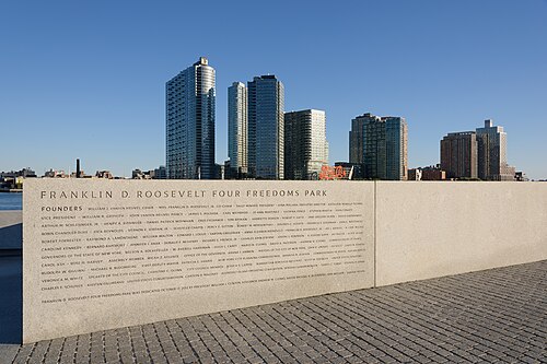 The inscribed granite wall at Four Freedoms Park on cobbled paving, with the Long Island City towers and the Pepsi-Cola sign across the water.