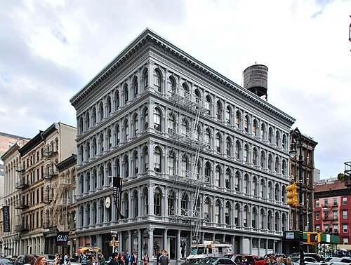 The E. V. Haughwout Building at Broadway and Broome Street, five floors of grey painted cast iron with arched windows between columns, a fire escape down one face and a wooden water tank on the roof.