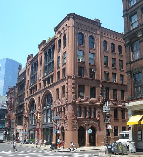 The corner of Wooster Street and Broome Street, a six floor building faced in red sandstone with round arches and heavy rusticated stone at the base.