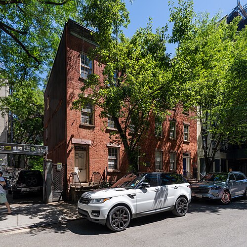 83 and 85 Sullivan Street, two small brick houses of two and a half floors with short stoops, under street trees in leaf.