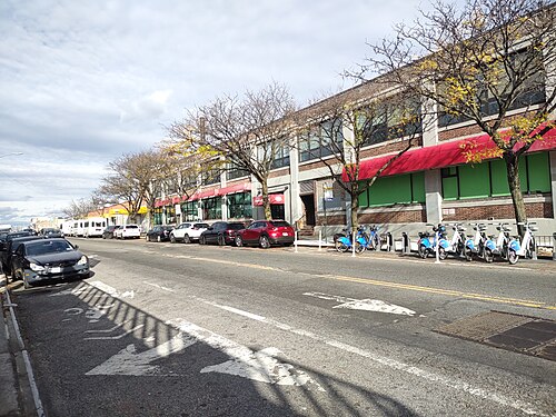 Lily Gavin Way, the Queens Boulevard service road between 39th Place and 40th Street, shops in a long two story building and a bike dock at the kerb.
