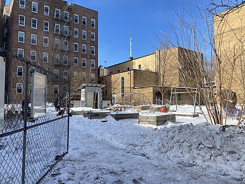 The community garden on 45th Street, raised beds under snow behind a chain link fence with apartment buildings over it.