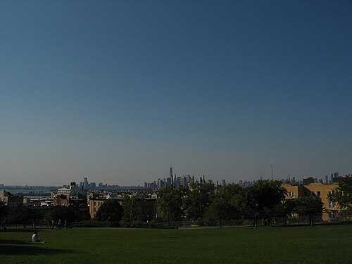 The lawn at the top of Sunset Park, rooftops below it and the Manhattan skyline along the horizon.