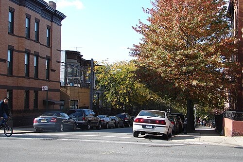 47th Street looking west from Sixth Avenue in the autumn, brick rowhouses with heavy cornices and cars parked down both sides.