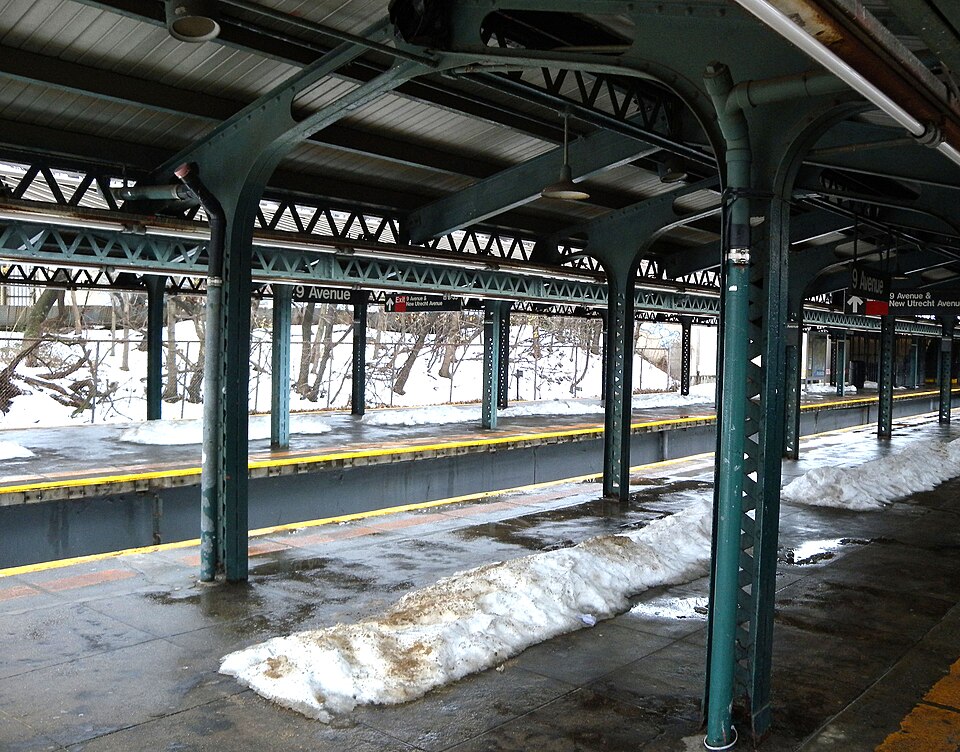 The northbound platform at Ninth Avenue under green ironwork columns and a canopy, snow on the ground beyond the tracks.