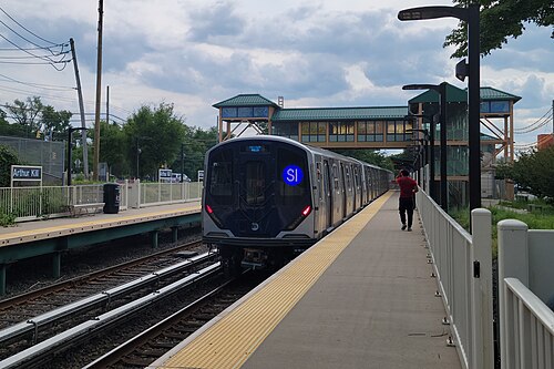 A train arriving at the Arthur Kill station on the Staten Island Railway, the covered overpass connecting the platforms behind it.