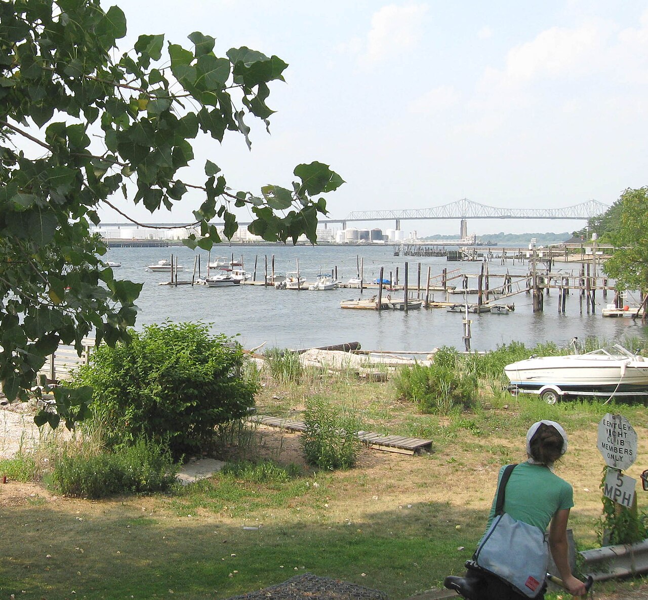 Looking north across the Arthur Kill from a yacht club near the foot of Bentley Street, moored boats at a small marina, the Outerbridge Crossing and the Perth Amboy, New Jersey shoreline in the distance.