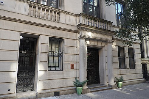 A limestone house front on East 68th Street with a columned doorway, an iron grille across the door and bars on the ground floor windows.