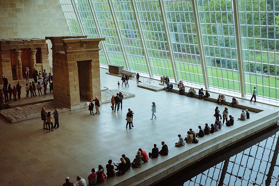 The Temple of Dendur and its gateway in the Sackler Wing at the Metropolitan Museum, seen from the balcony, with the sloping glass wall along the far side and the reflecting pool in the corner.