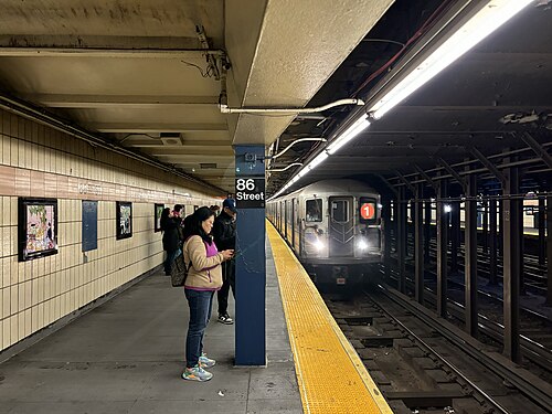 The southbound platform at 86th Street on the 1 line, tiled wall with the station name set in mosaic and a train coming in.