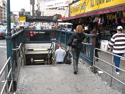 The street stair down to the 181st Street station on the 1 line, with a gift shop's awning and hanging goods over the sidewalk beside it.