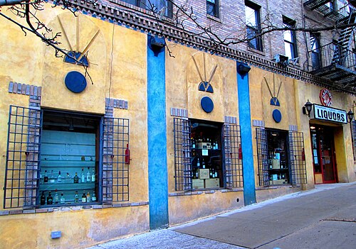 A liquor store front on West 181st Street, yellow stucco with blue pilasters and plaster fans over the barred windows.