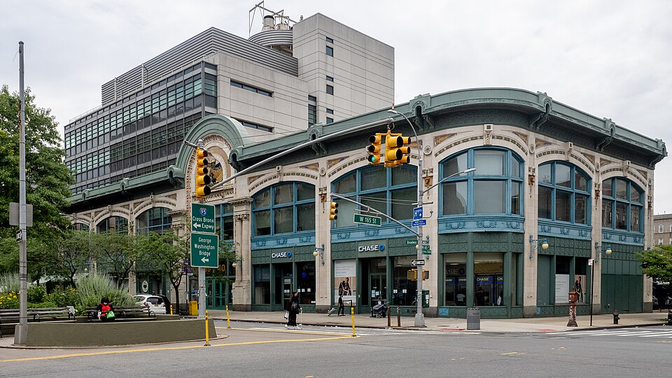 The kept front of the Audubon Ballroom at 3940 Broadway, arched windows under a green cornice, with a bank branch at street level and a Columbia research building behind it.