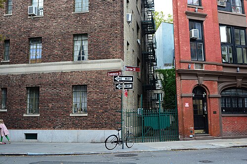The corner of Commerce Street and Barrow Street, worn brick on one side and a red front with an arched doorway on the other, with a green gate across a private alley between them.