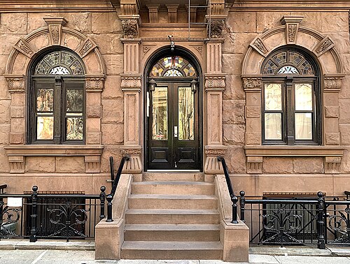 The doorway of 266 West 11th Street, rough faced brownstone with carved capitals and a stained glass fanlight over the double doors.