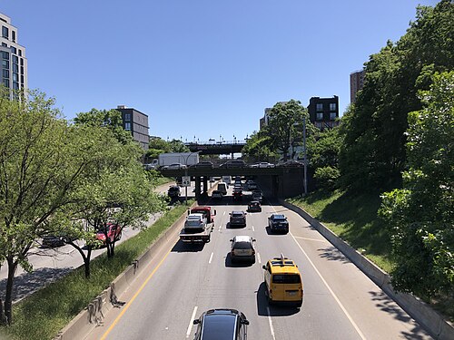The Brooklyn-Queens Expressway in its open cut, seen west from the South 4th Street overpass, with trees down both banks and apartment buildings above them.