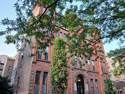 The Long Island Business College Building, four storeys of red brick and brownstone with an arched entrance, one bay covered from top to bottom in ivy.