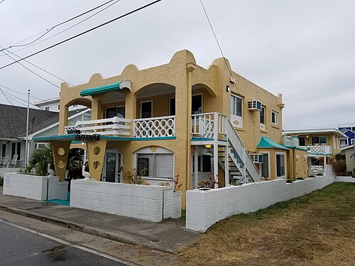 A two storey yellow stucco Art Deco building with rounded parapets, white lattice balustrades, exterior stairs and pelican statues flanking the entrance.