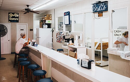 The counter inside Britt's Donuts, a neon Britt's sign and a Since 1939 sign on the wall, blue vinyl stools along a white laminate counter.
