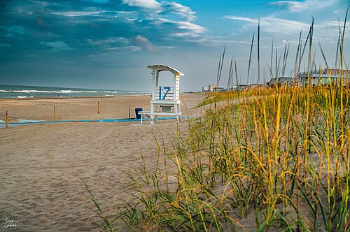 A numbered wooden lifeguard stand behind dune grass, a sand path leading down to the waterline.