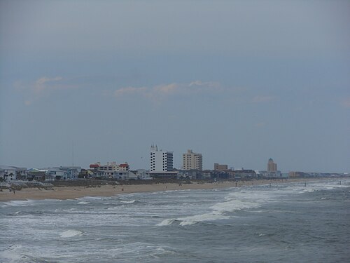 A distant view down the beach toward a cluster of mid rise condo towers behind the dune line.