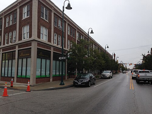 A three storey brick corner building with bank signage in its windows, Detroit Avenue receding past parked cars and street trees toward the theatre block.