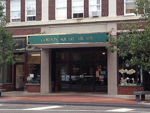 The Gordon Square Arcade entrance, a green awning over glass doors between storefronts, with apartment windows and stone trim above.