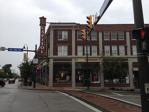 The Capitol Theatre's vertical marquee and rounded brick corner from West 65th Street, storefronts and a flag hung below the sign.
