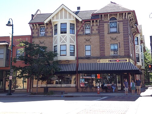 A gabled Tudor style building with storefronts under a striped awning, bay windows and patterned brick above.