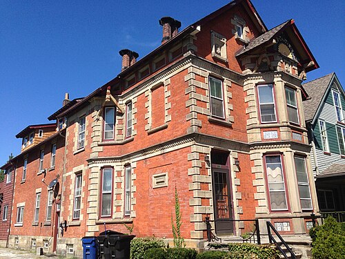 A red brick Victorian house on West 58th Street with stone quoins, a projecting bay window and decorative gable trim.