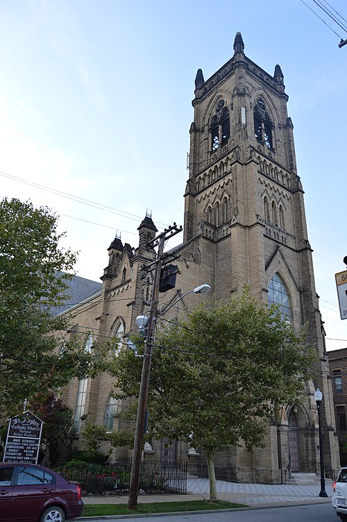 St. Stephen Church's Gothic stone bell tower, arched windows and lancet openings rising above street trees and a power line.