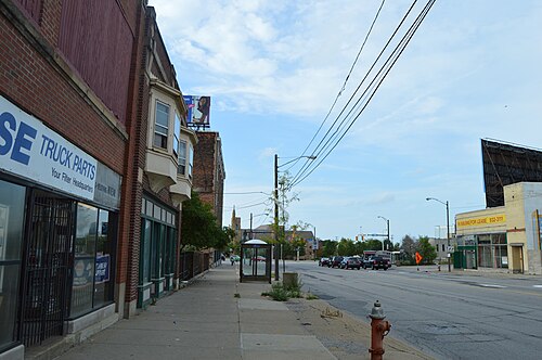 West 25th Street looking north toward the Detroit Avenue intersection, a corner truck parts store and a distant church spire past the billboards.