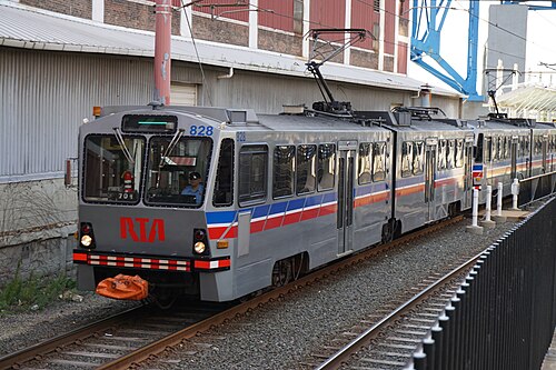 An RTA light rail car running past a corrugated metal and brick warehouse building.