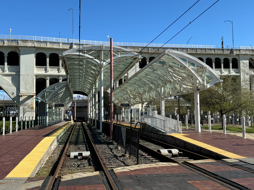 The Waterfront Line platform under a curved glass canopy, with the Detroit-Superior Bridge's concrete arches behind it.