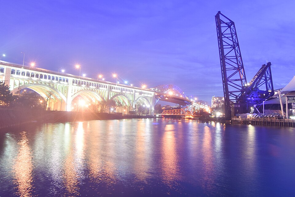 The raised railroad lift bridge and the Detroit-Superior Bridge seen from Settler's Landing Park on the east bank, lit at dusk.