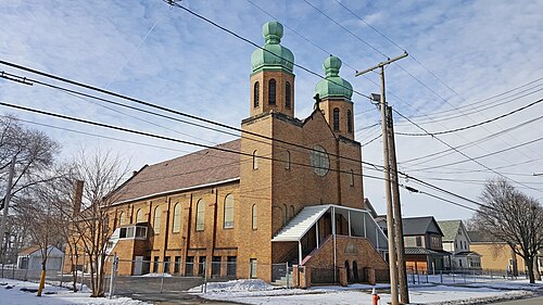A yellow brick church on West 11th Street with twin towers under green onion domes and a covered exterior stairway to the entrance.