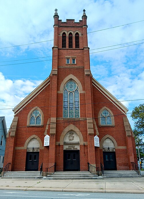 A red brick Gothic Revival church tower on Scranton Road, pointed stained glass windows and paired black doors under stone arches.