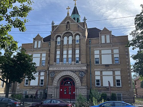 A three storey tan brick Romanesque school on Professor Avenue, arched windows, a small corner spire, and a Northeast Ohio College Preparatory School banner over the door.