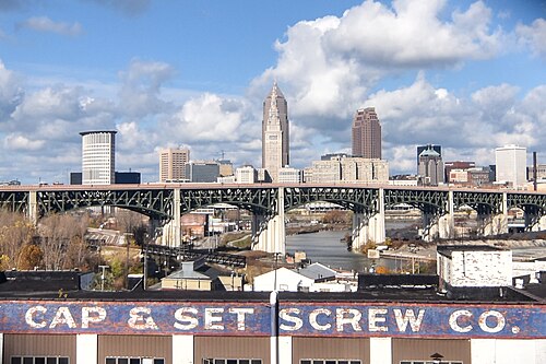 Downtown Cleveland's Terminal Tower and Key Tower behind a green steel arch bridge, a painted CAP AND SET SCREW CO. sign on a warehouse roof in the foreground.