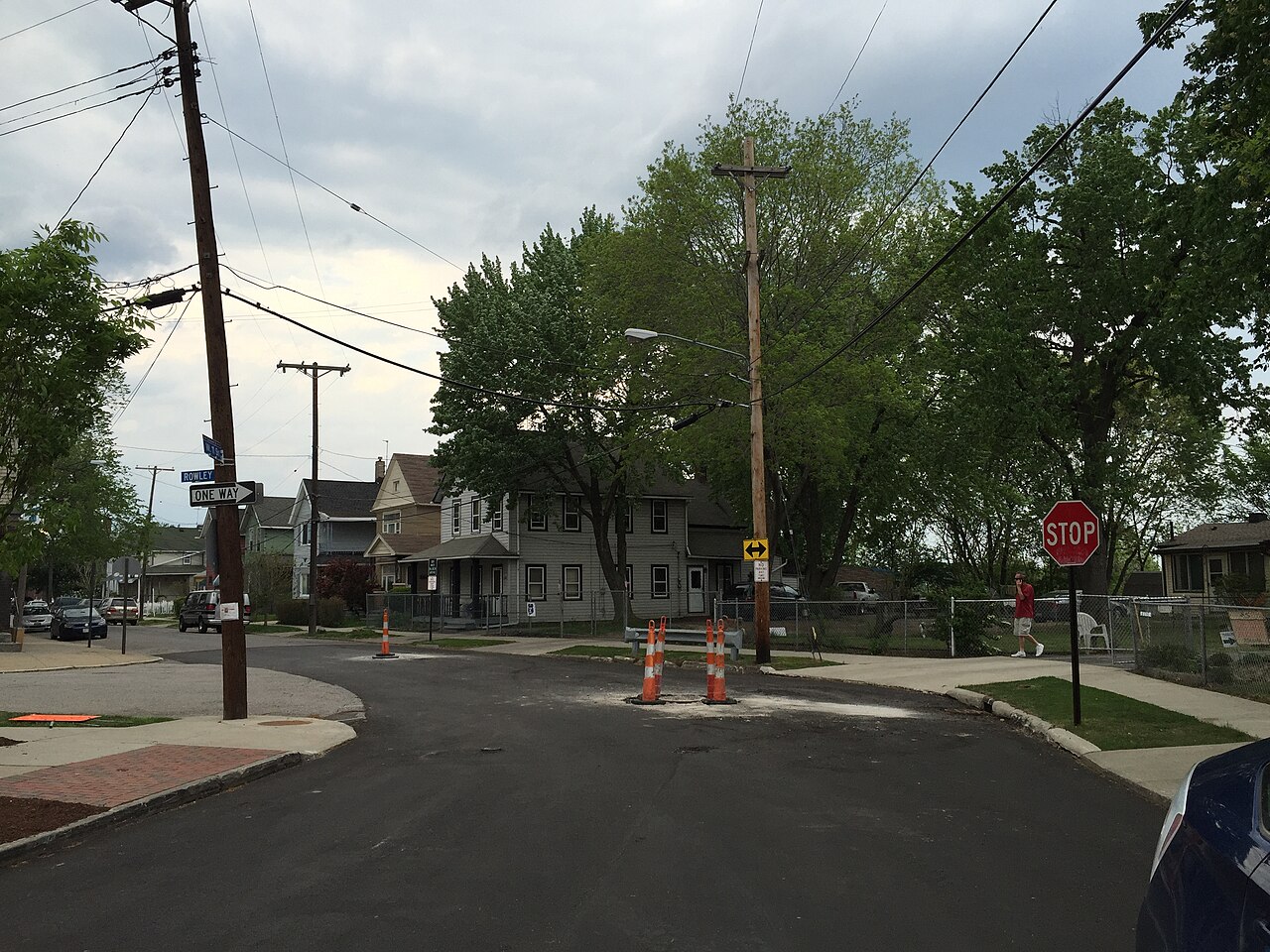 A residential street bend on West 11th Street, two storey wood frame houses, a stop sign, utility poles and overhead wires.
